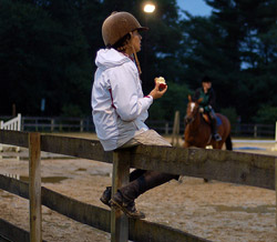 Assistant trainer sitting on a fence eating an apple