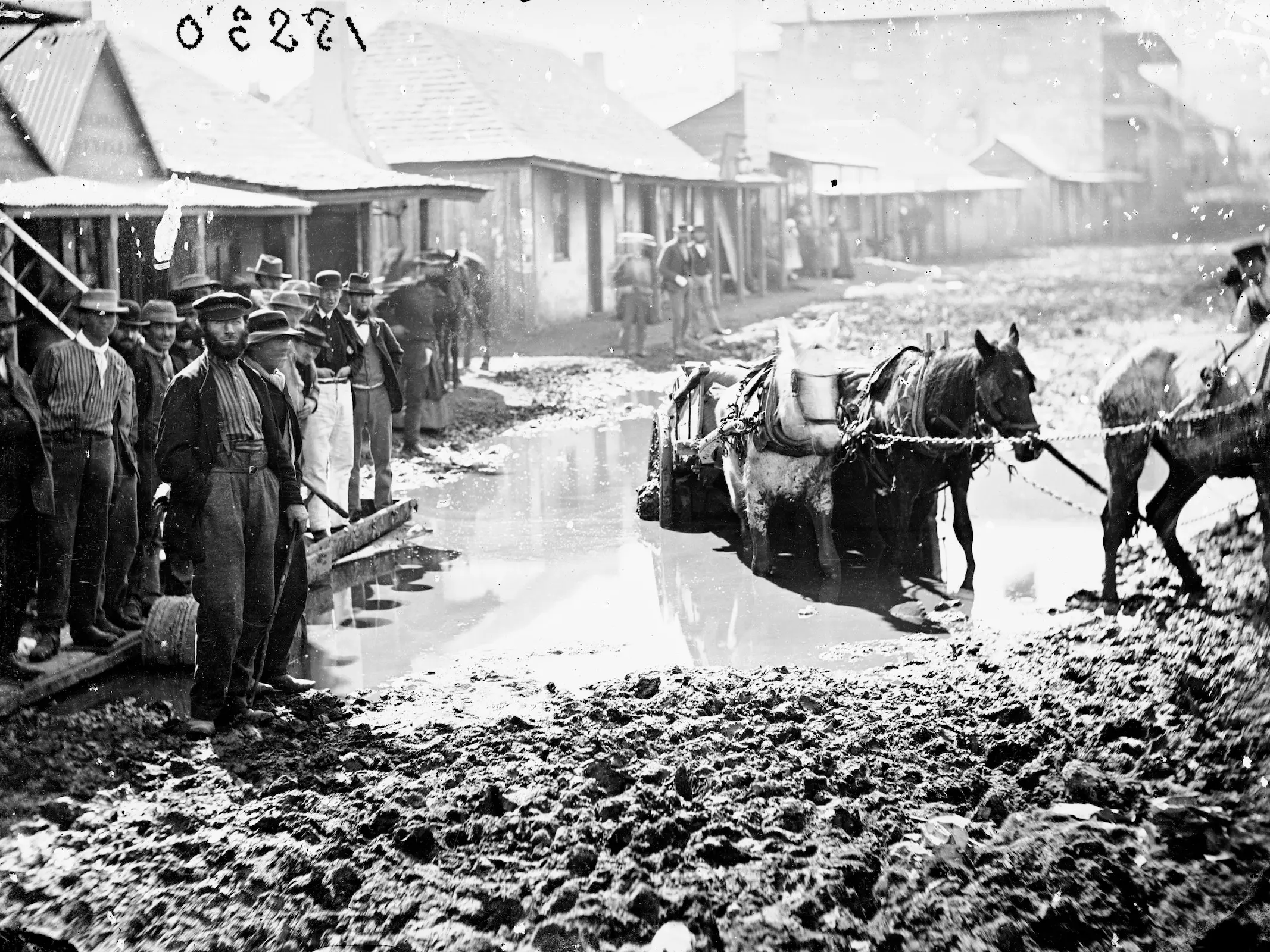 Horses pulling a wagon that is stuck in the mud