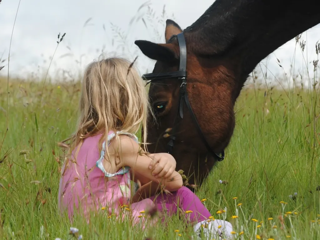 A child sitting next to a grazing horse